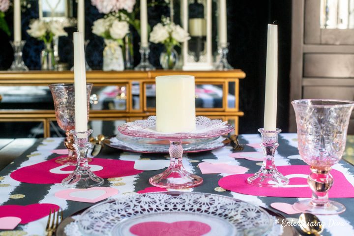 Valentine Day table centerpiece with pink glass cake stand, white candles and paper hearts