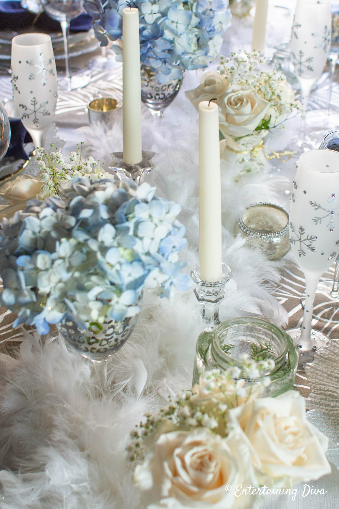 Tall white candles in glass candlesticks as part of winter wonderland centerpiece