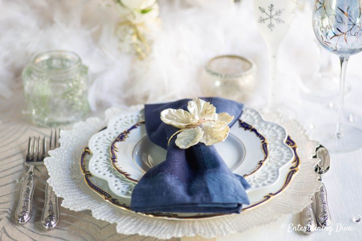 White glass charger, blue and gold-edge plates and blue napkins on a winter wonderland tablescape