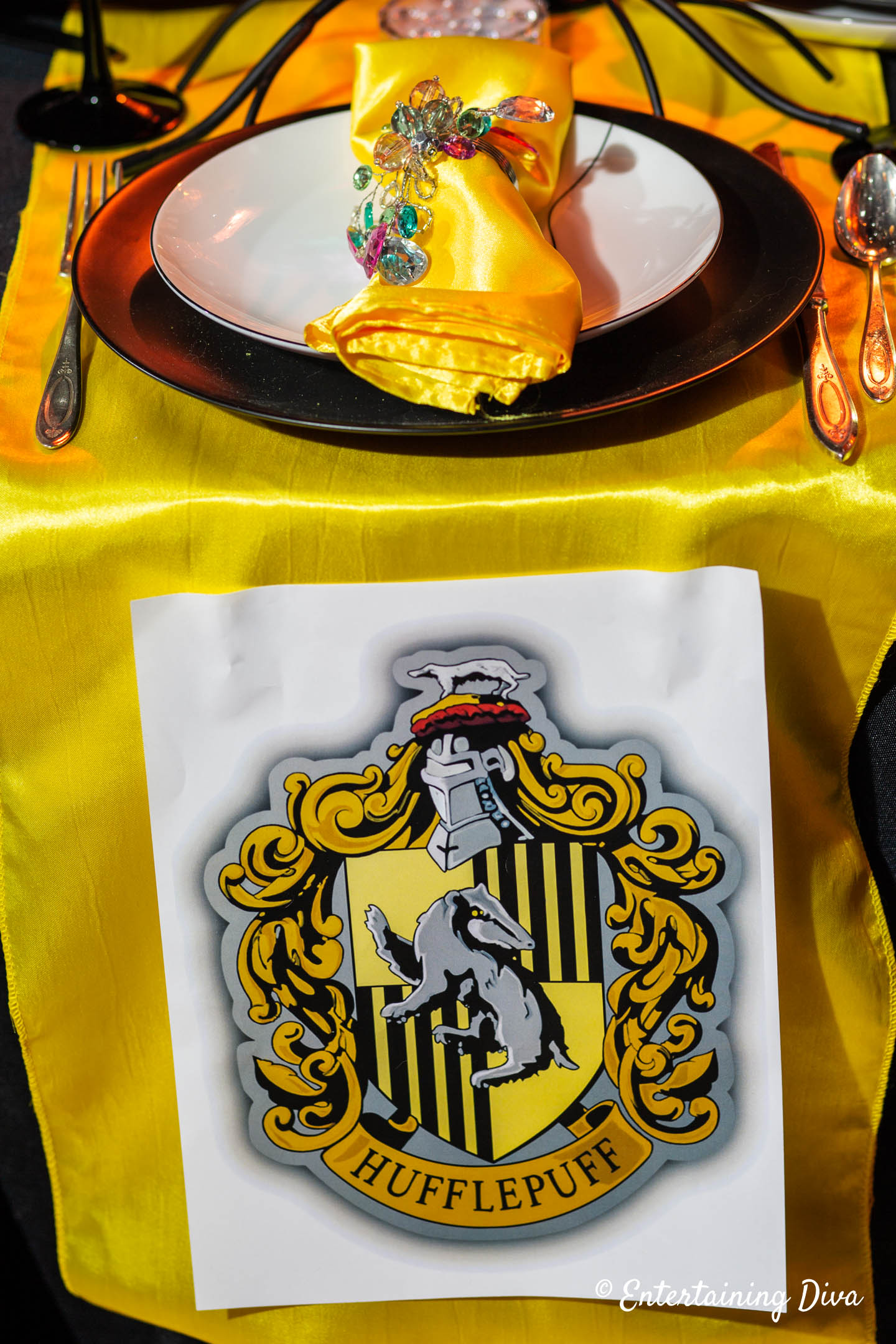 Yellow napkin on black and white plates with a table runner that has the Hufflepuff crest