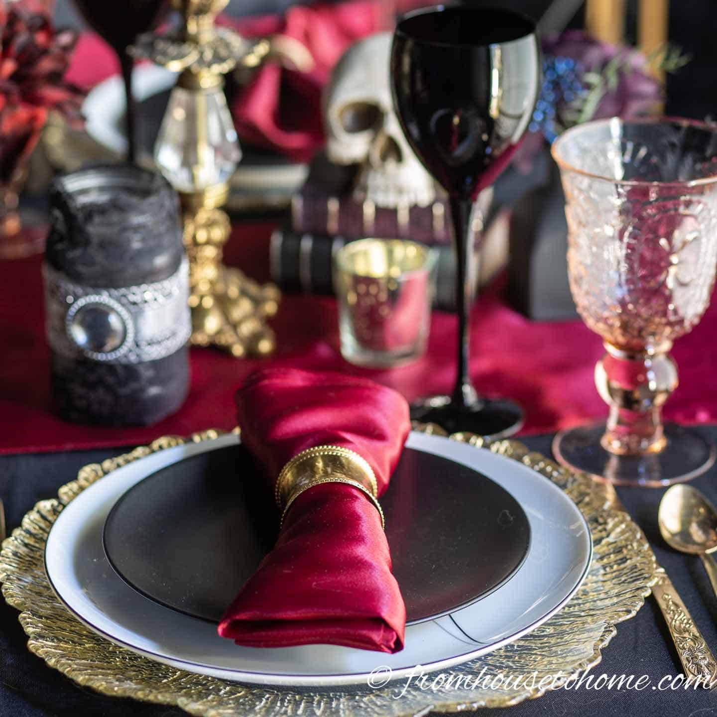 Halloween table setting with black plates, red table runner and gold charger
