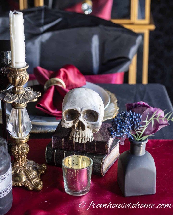 Halloween centerpiece with a vintage gold candlestick, a skull on old books and a black vase