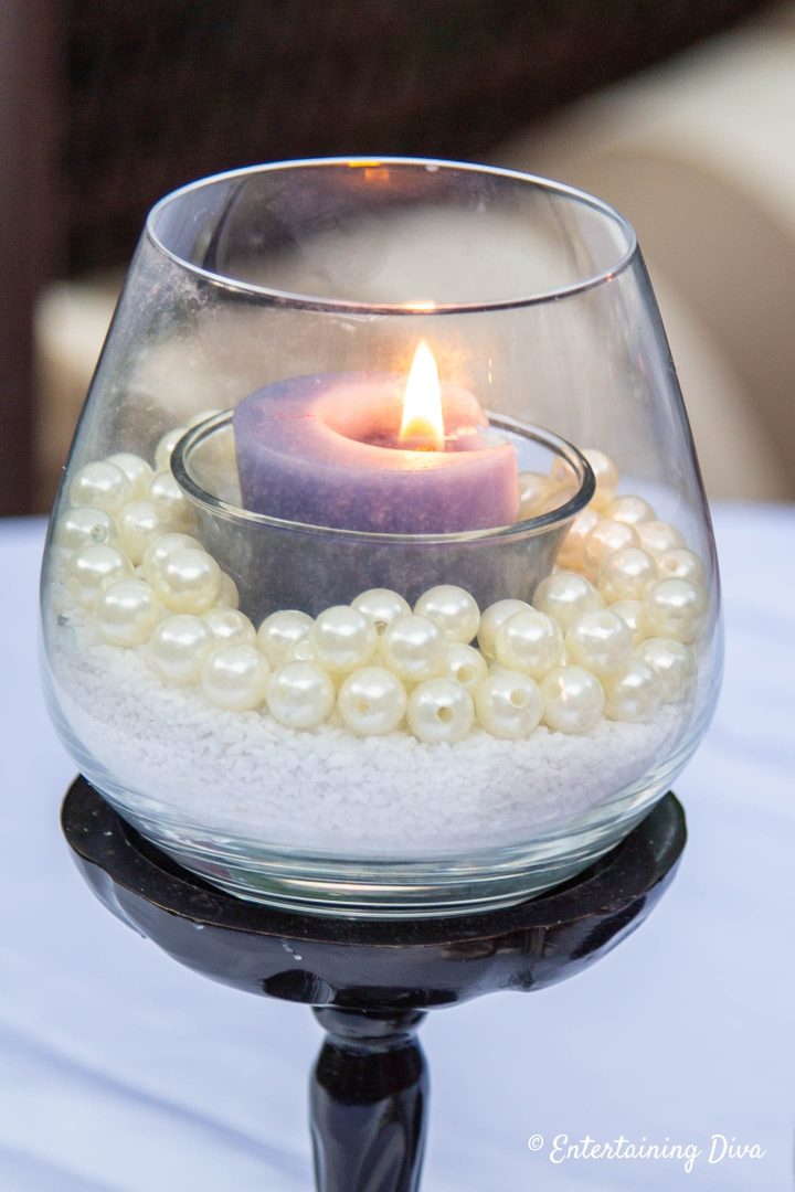 Stemless wine glass made into a candle holder with white sand, faux pearls and a blue votive candle