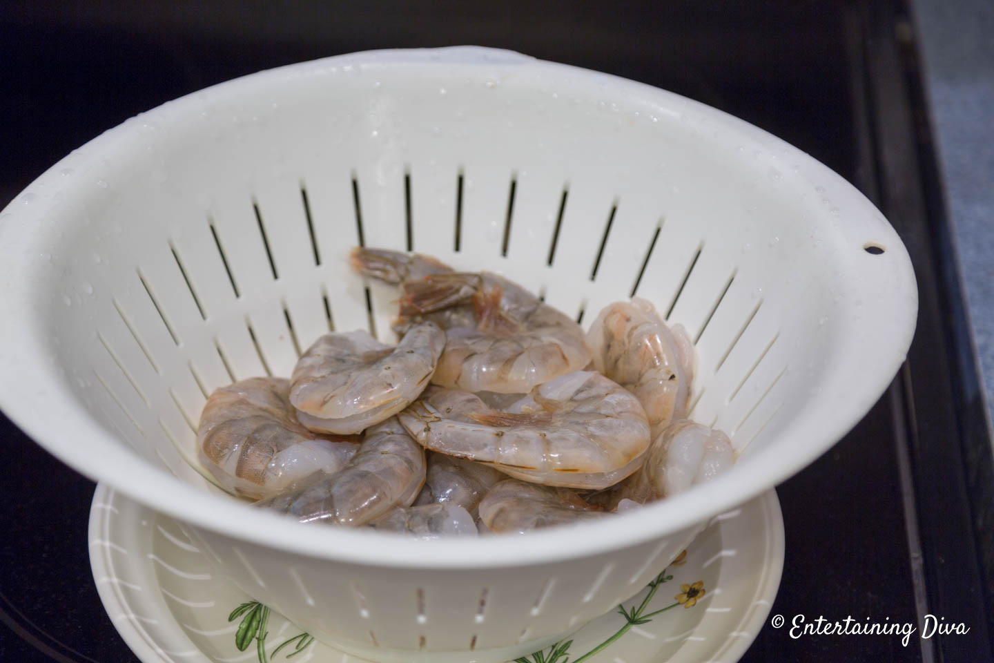Uncooked frozen shrimp being thawed in a colander