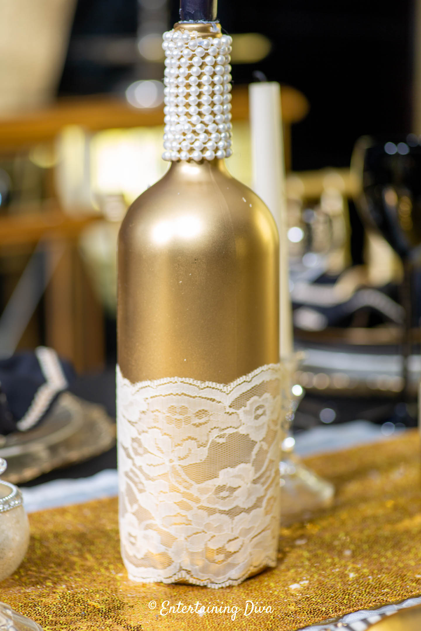 Decorated gold wine bottle with white lace around the bottom and pearls around the neck