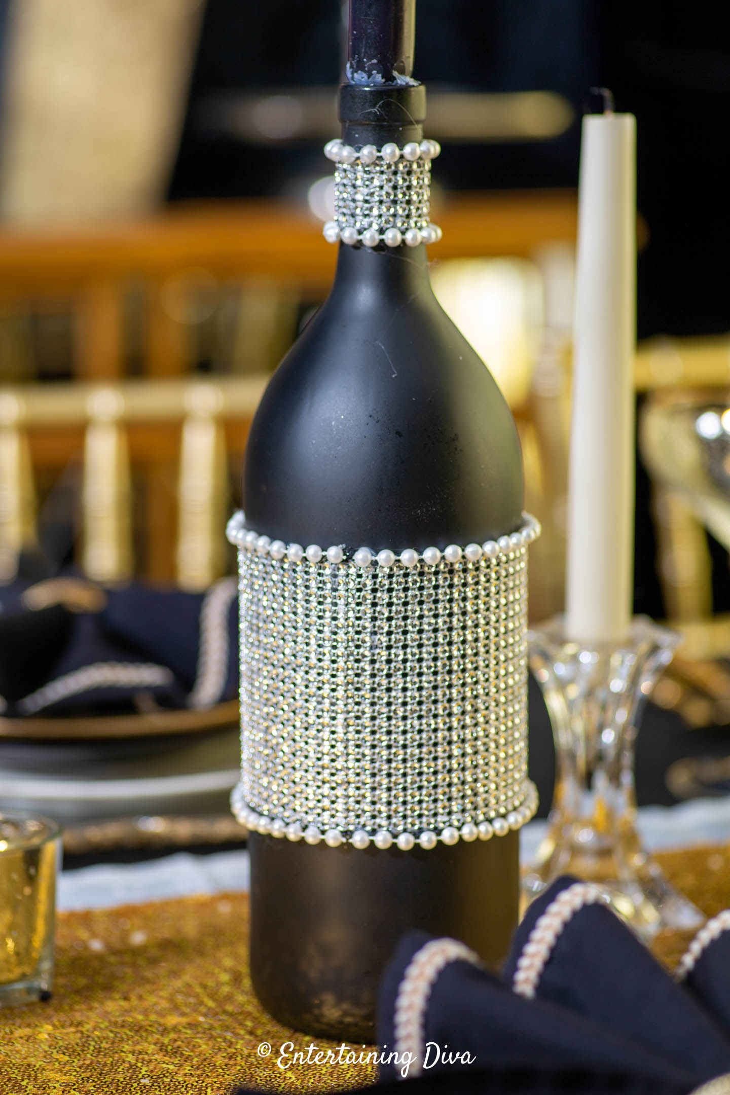 Decorated black wine bottle with rhinestone ribbon and pearls around the middle and the neck of the bottle