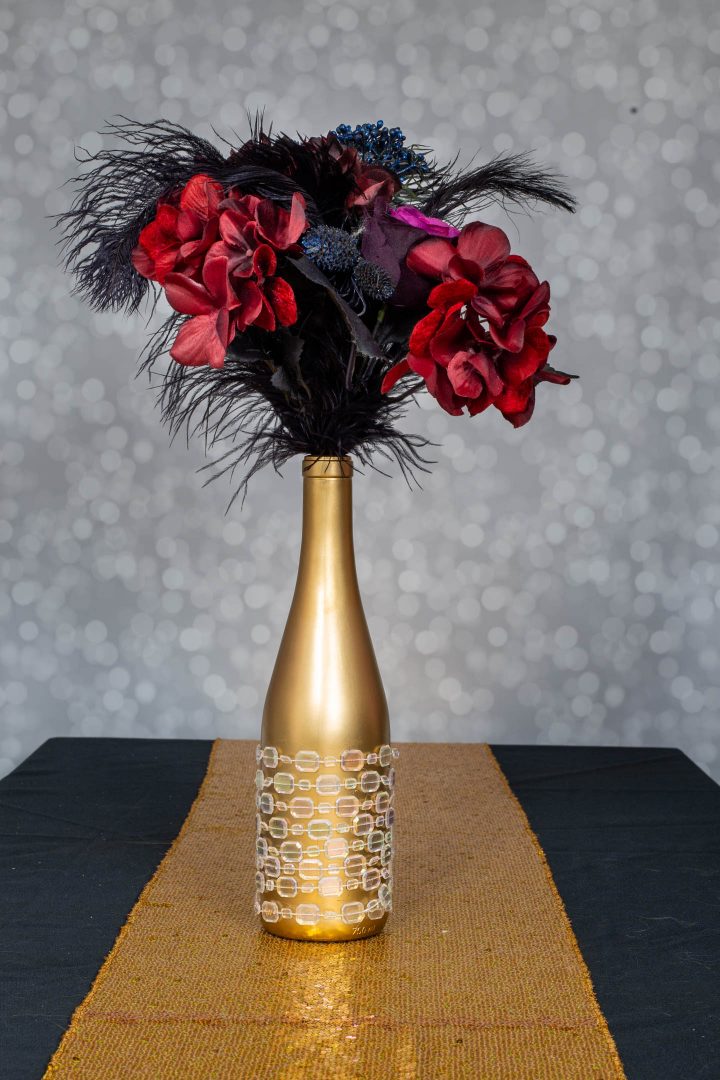 Embellished wine bottle centerpiece with faux flowers and black ostrich feathers