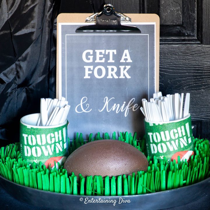"Get a fork & knife" clipboard sign on a tray with Touch Down cutlery holders, a football and fake grass