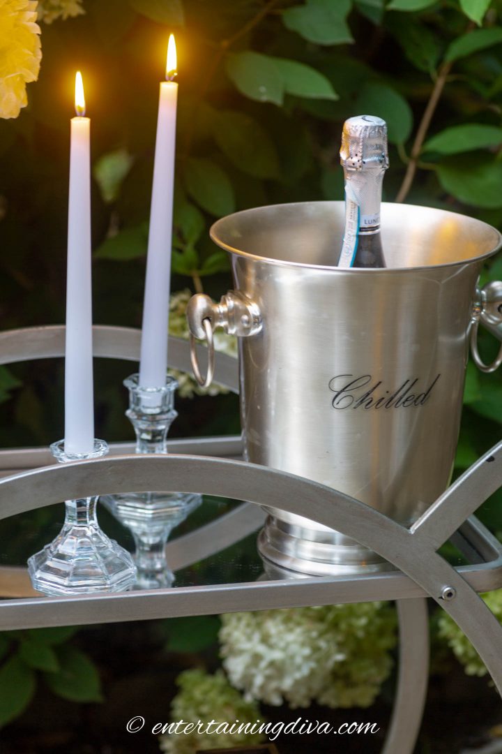 Candles and an ice bucket with champagne on a bar cart outside