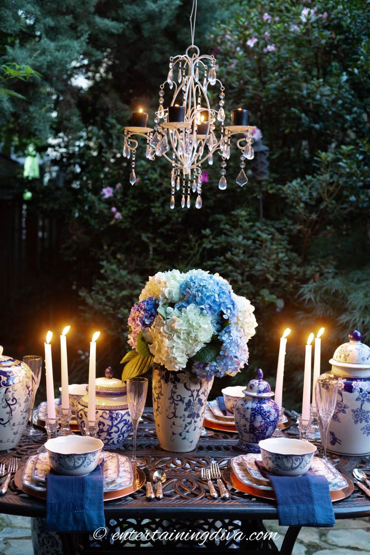 Blue and white outdoor tablescape with a candle chandelier hung above the table