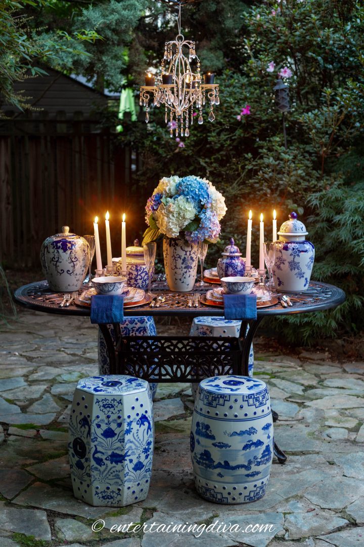 Blue and white outdoor dinner party table setting with garden stools and a white candle chandelier