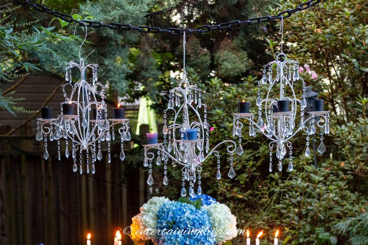 Three white candle chandeliers hung over an outdoor tablescape