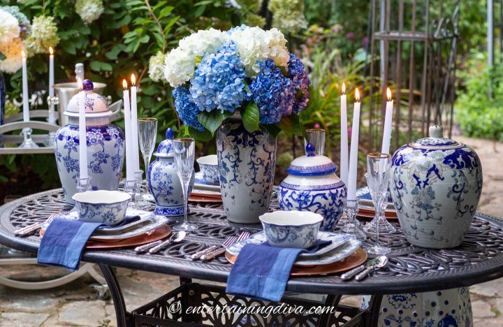 Blue and white outdoor dining table centerpiece made with ginger jars, flowers and candles