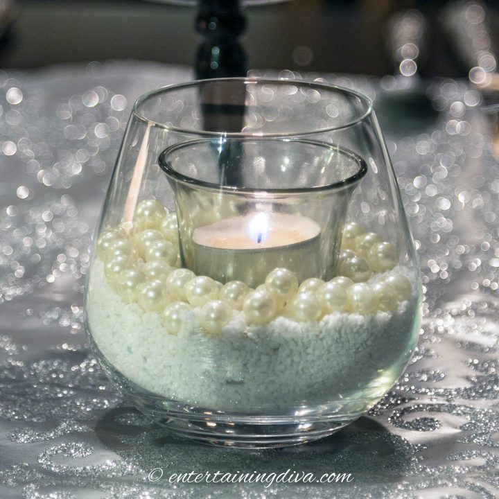 A Christmas candle holder made from a stemless wine glass filled with sand and faux pearls 