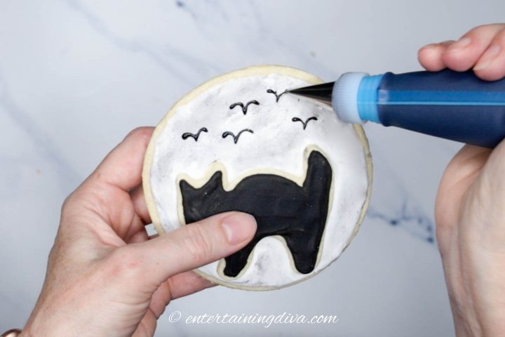 Bird silhouettes being piped on the cat silhouette cookie