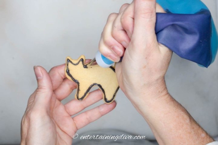 Black outline being piped onto black cat cookie