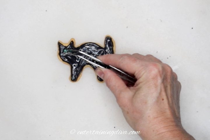 Green sugar pearl eyes being added to decorated black cat sugar cookie