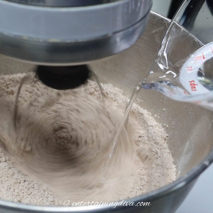 water being added to icing sugar, meringue powder and cocoa powder in a mixing bowl