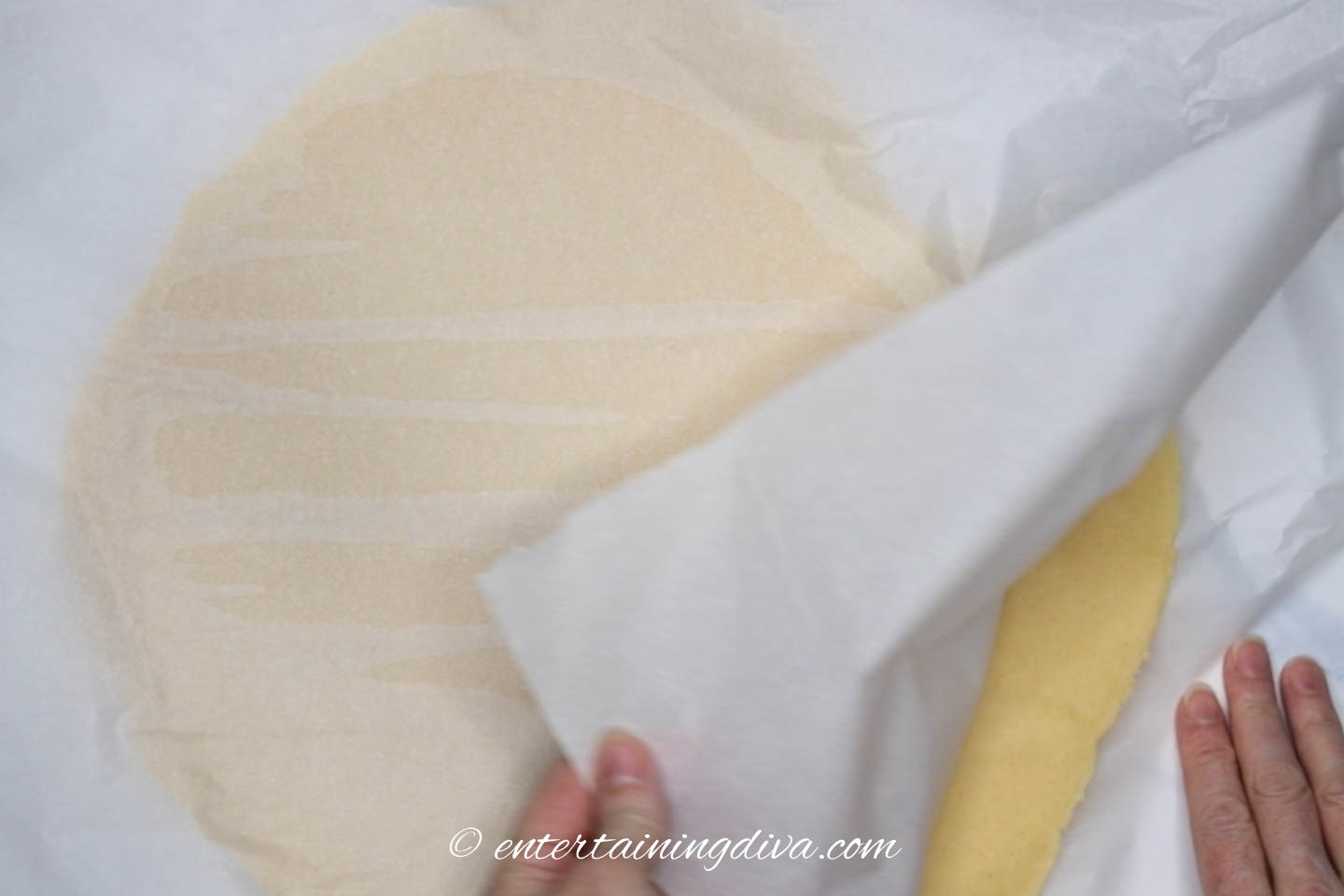 Parchment paper being taken off chilled, rolled-out cookie dough