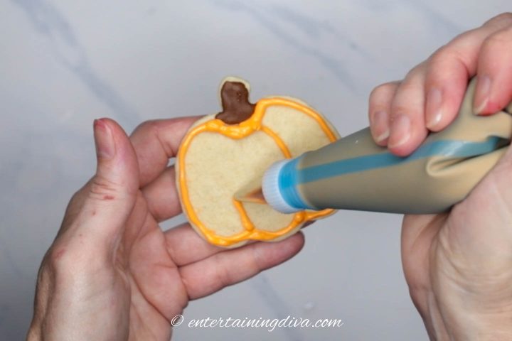 Orange royal icing lines being added to the middle of the pumpkin cookie
