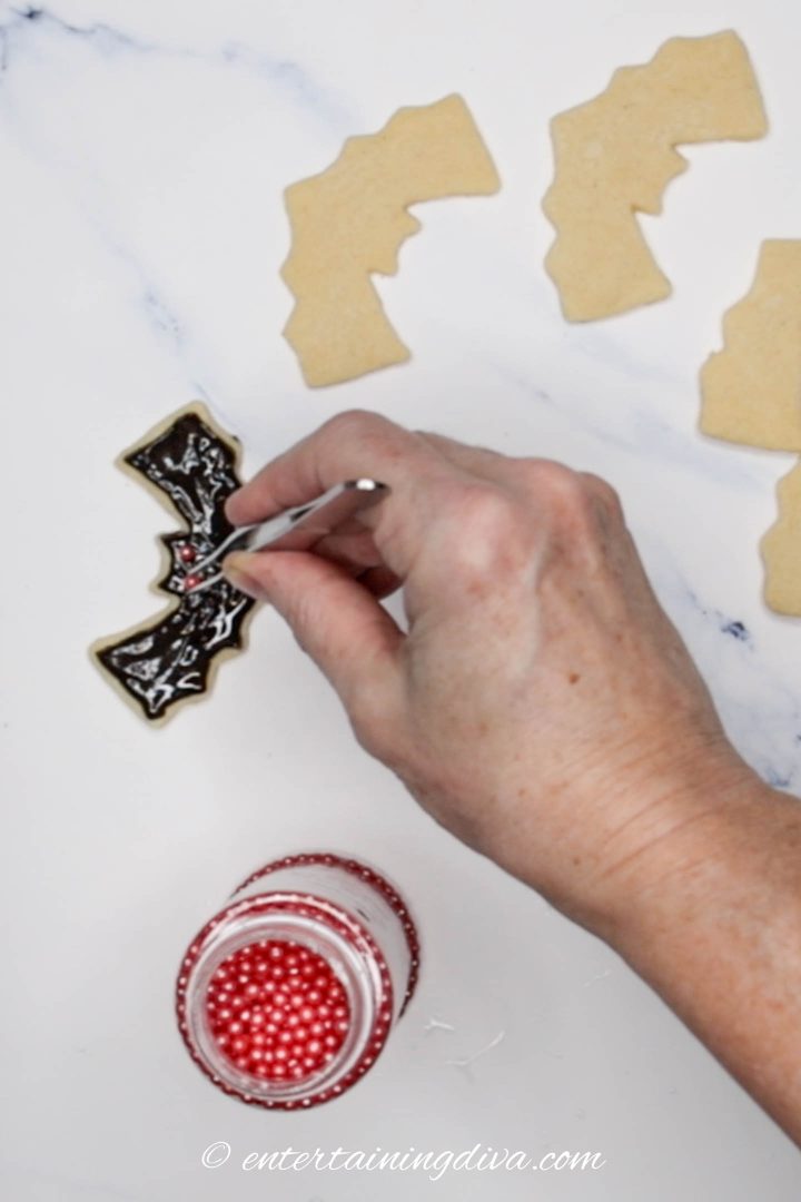 Red pearl eyes being added to the frosted Halloween bat sugar cookie
