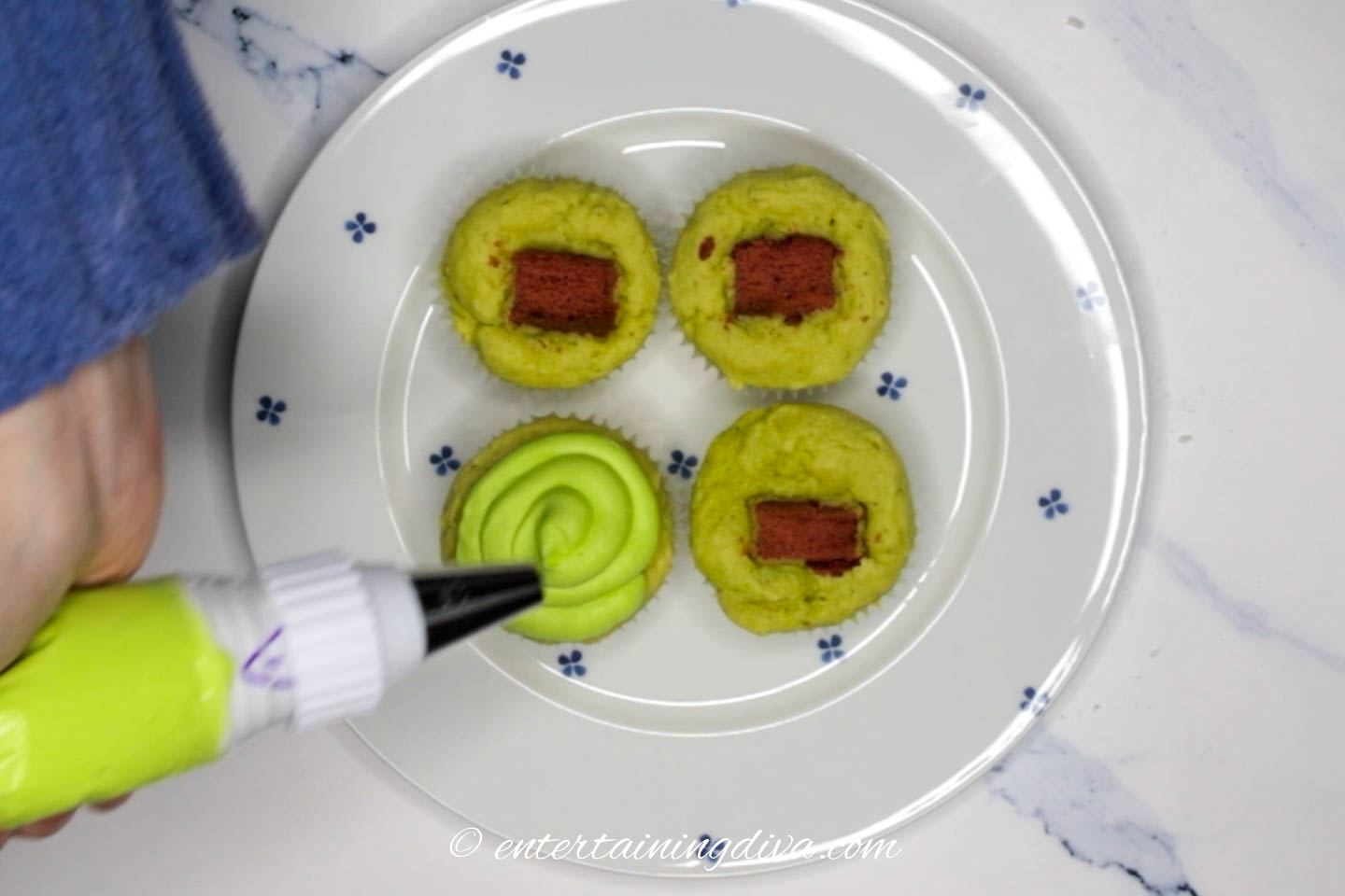 Green icing being piped onto the top of the cupcakes with hearts in them
