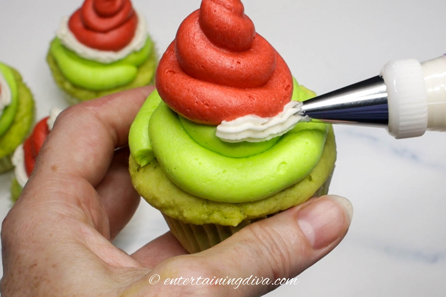 White icing being piped around the bottom of the red Santa hat icing