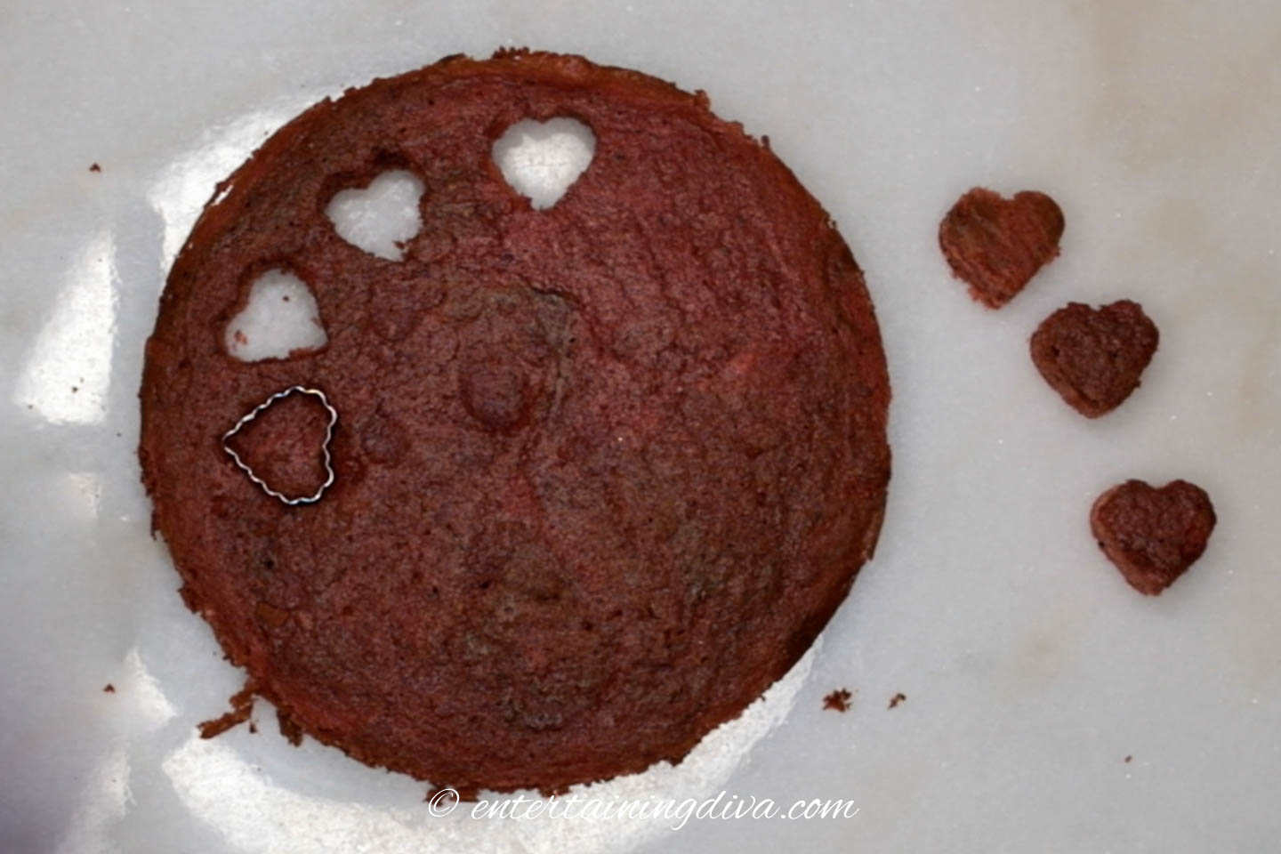 small hearts being cut out of a red velvet cake layer