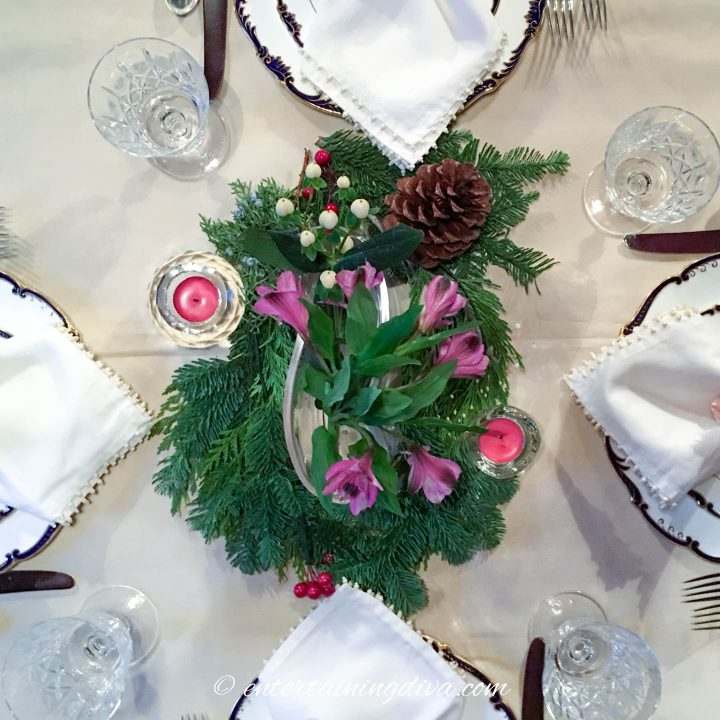DIY Christmas centerpiece made with evergreen branches, pine cones, purple flowers and tealight candles in crystal candle holders