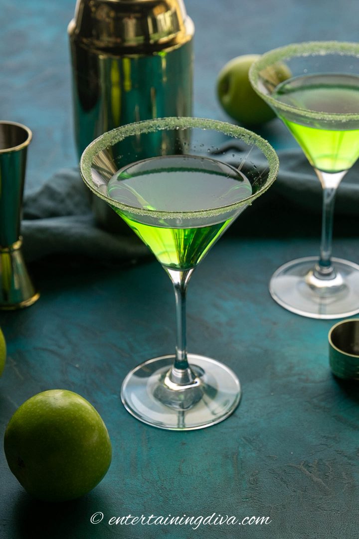 apple martini on a blue green background with a cocktail shaker