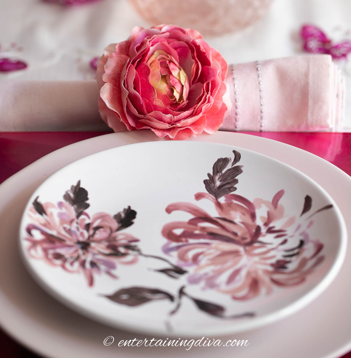 Pink napkin with a floral napkin holder behind a pink place setting