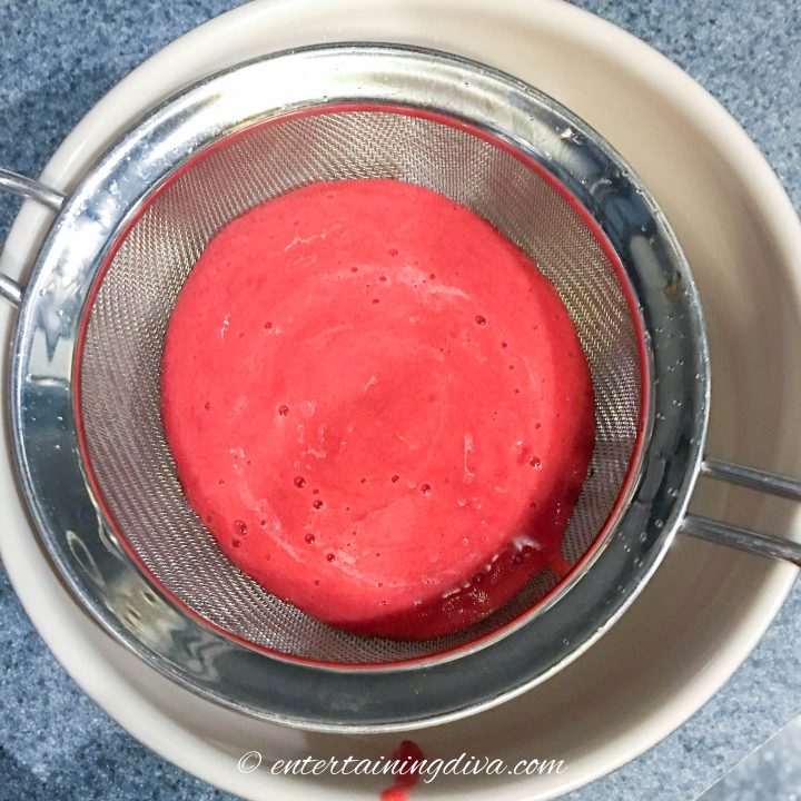 Homemade raspberry sauce in a sieve over a bowl