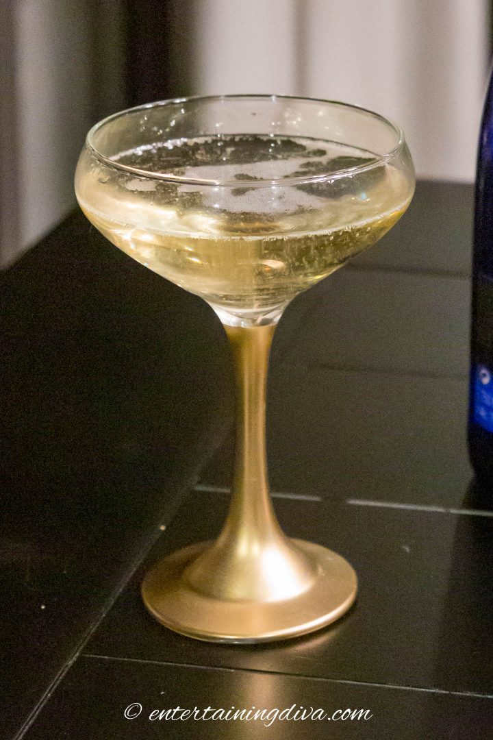 A painted gold-stemmed coupe glass with champagne in it
