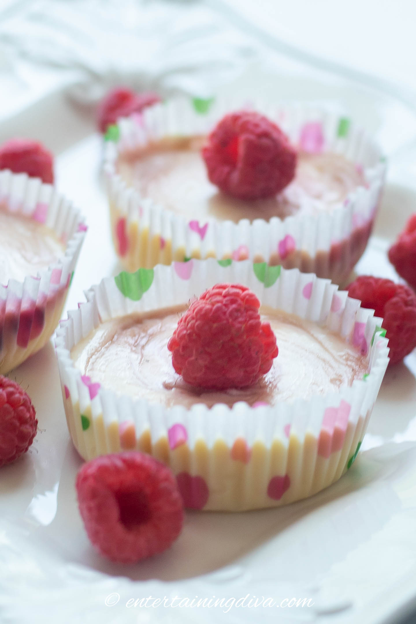 mini raspberry cheesecakes on a plate with raspberries