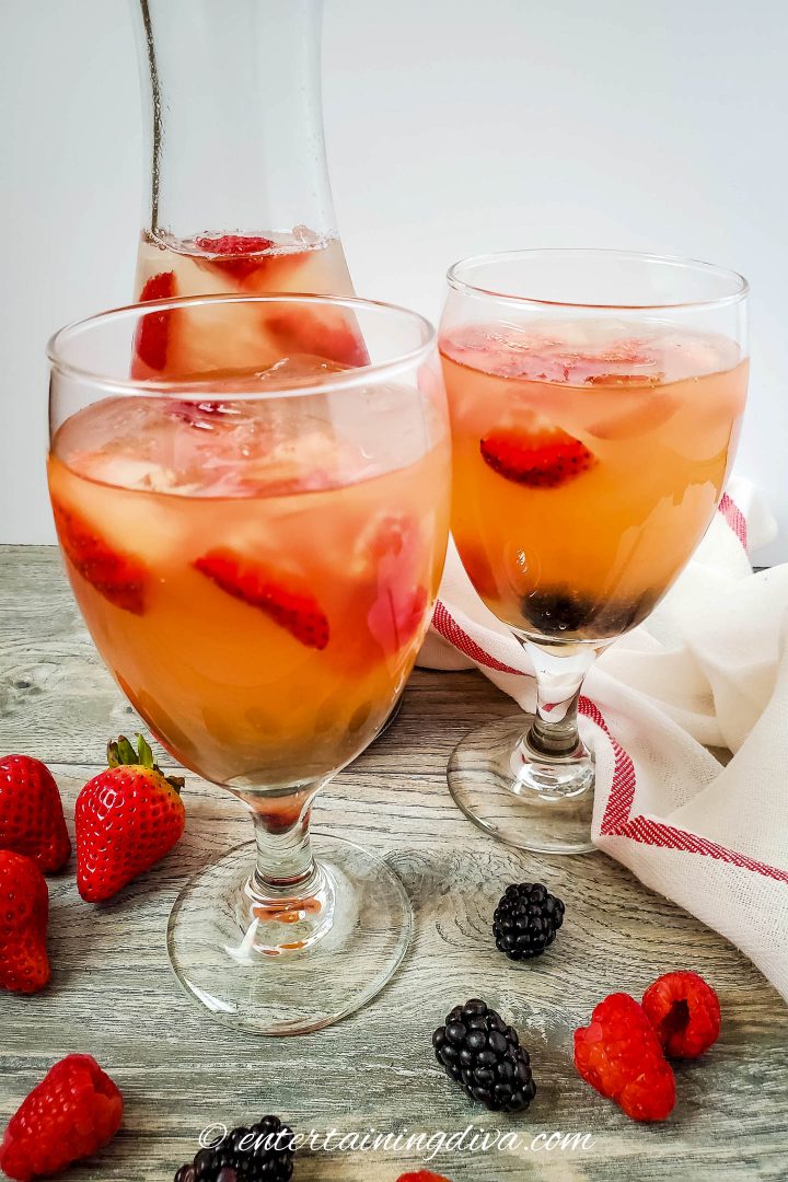 two glasses and a pitcher of triple berry rose sangria with fruit and ice