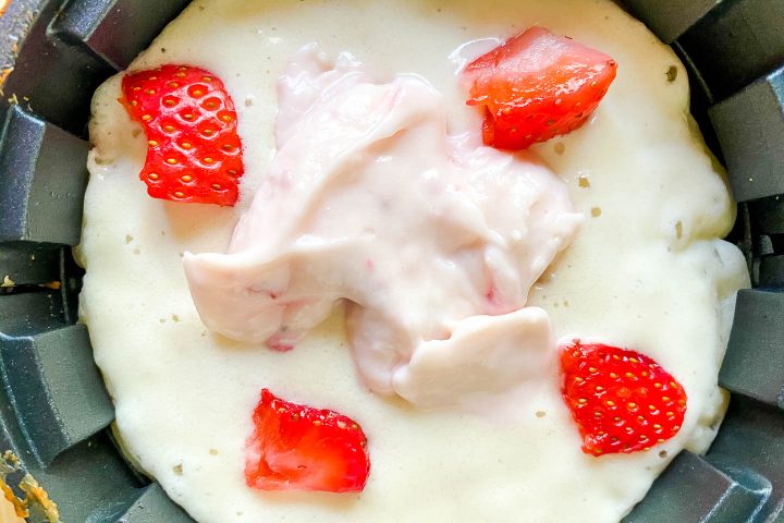 The strawberry cheesecake layer on top of the waffle batter in a waffle iron