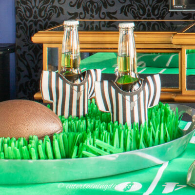 A football and two beer bottles in referee koozies on a football field tray