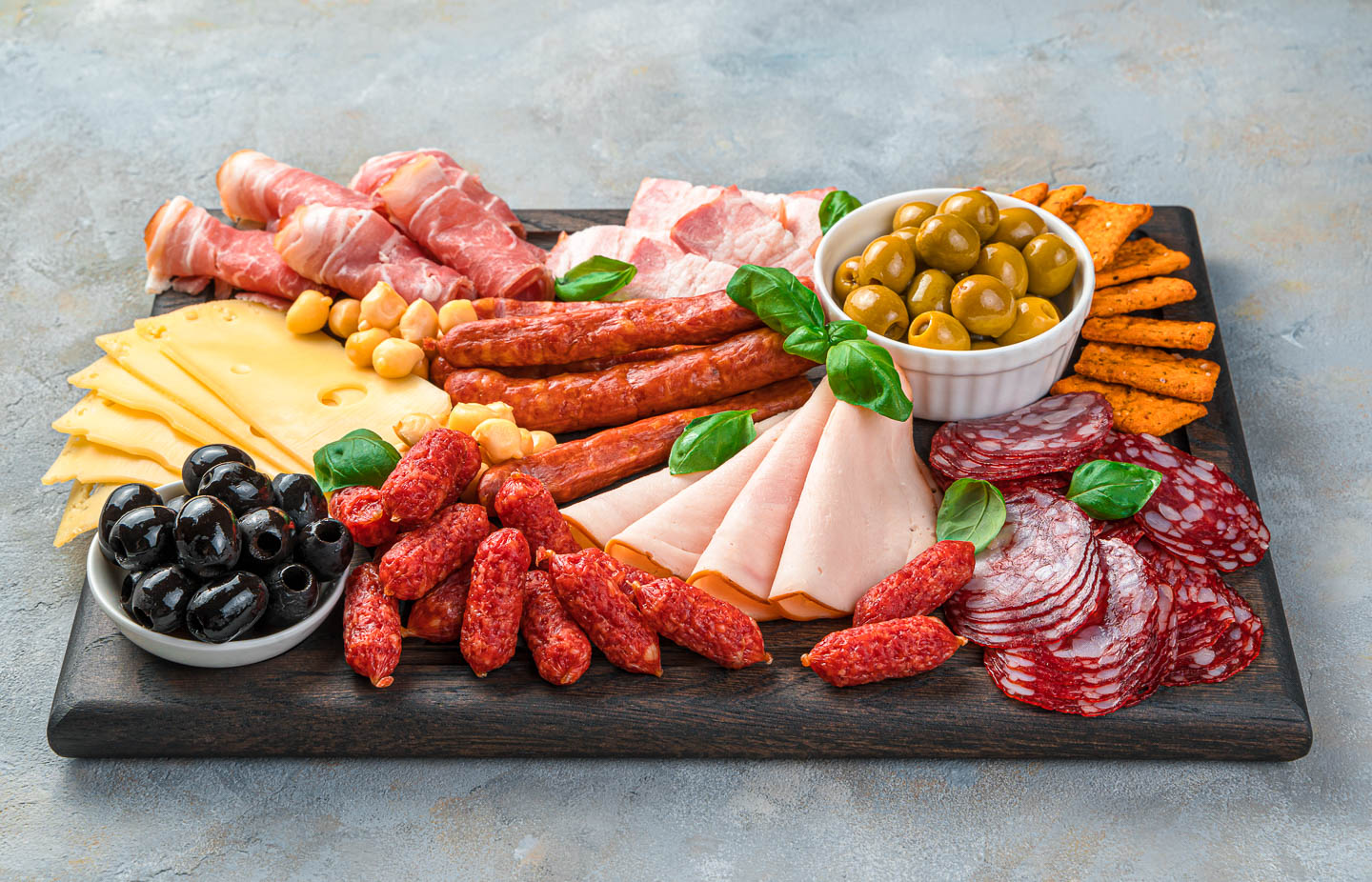 two bowls filled with olives on a rectangular charcuterie board with various meats and cheeses