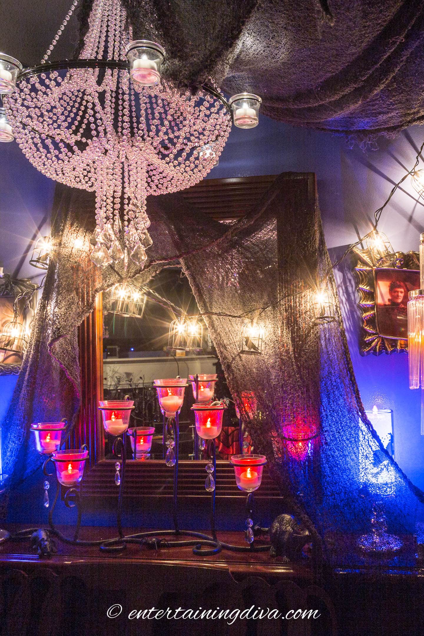 A mirror and chandelier draped with creepy cloth and Halloween lighting
