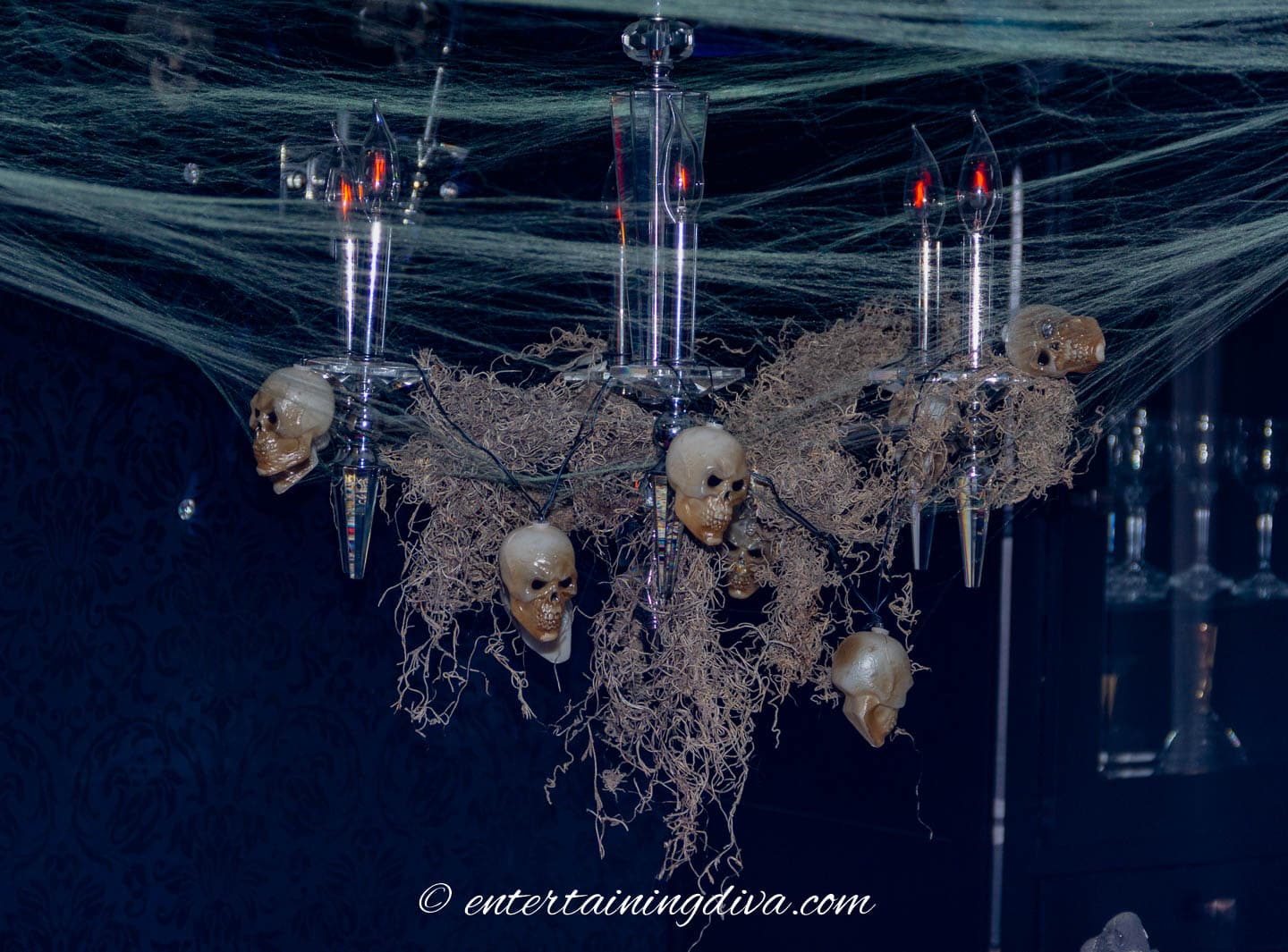 stretchy spider web around a chandelier decorated for Halloween with Spanish moss and skulls