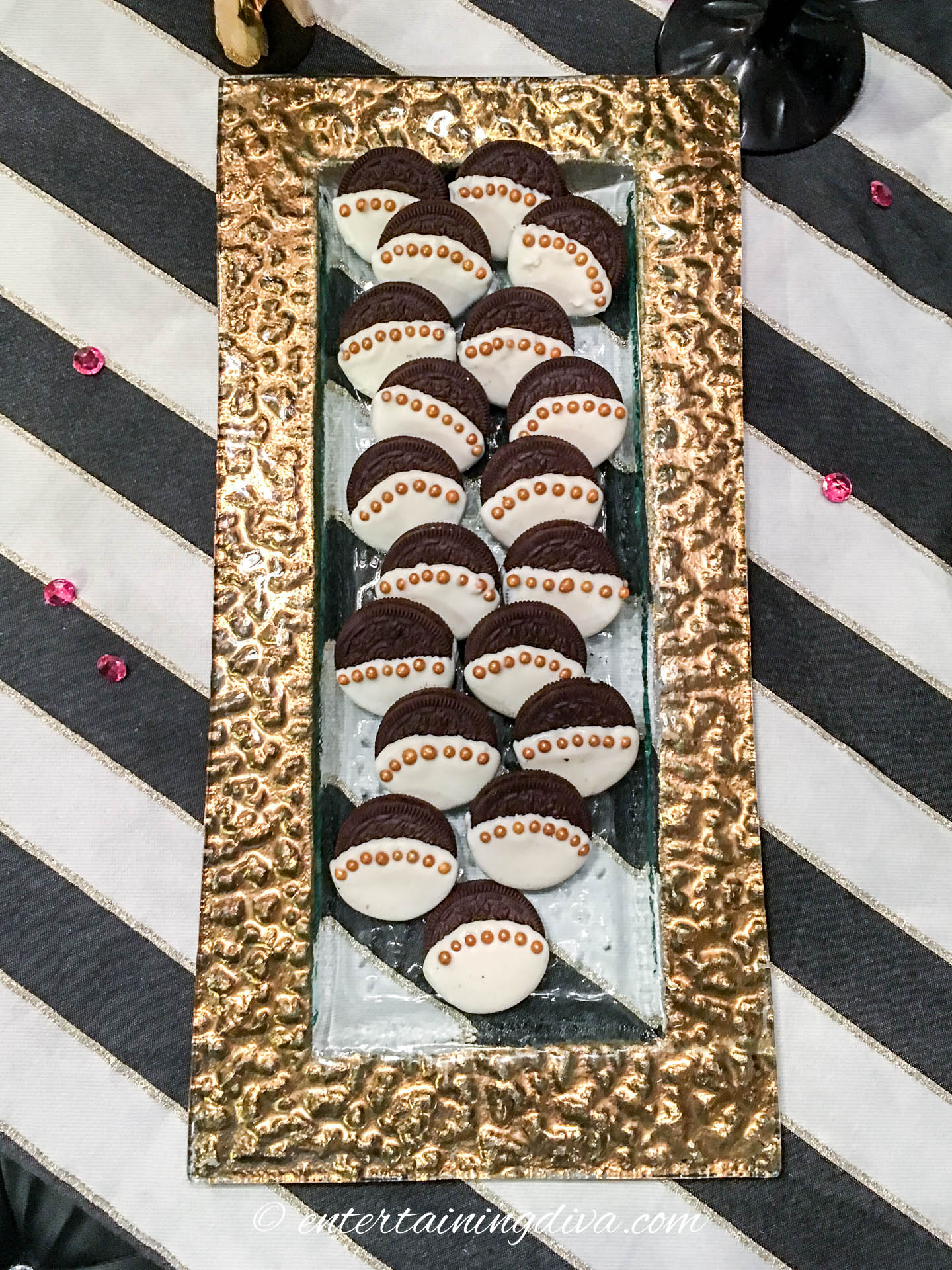 A tray of gold trimmed white chocolate covered Oreo cookies on a black and white table cloth