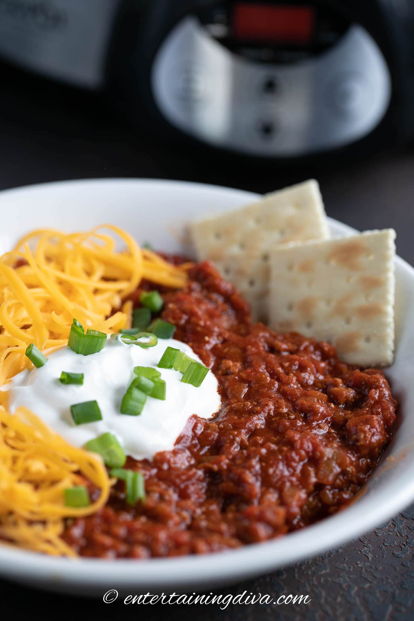 Close up of slow cooker no bean chili in a bowl with sour cream, green onions, grated cheese and crackers