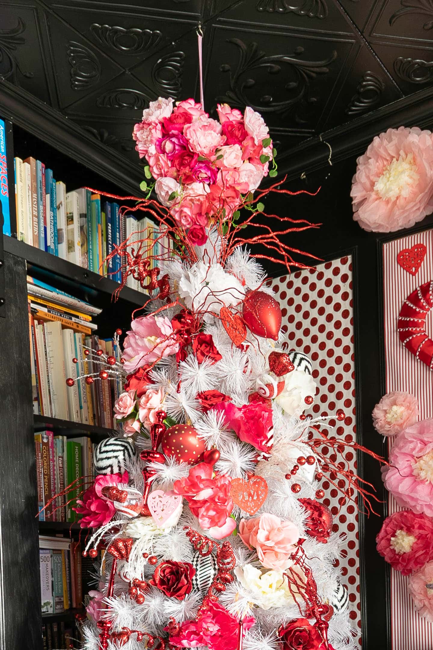 Heart shaped Valentine tree topper covered in pink and red roses hung from the ceiling above a Valentine's Day tree