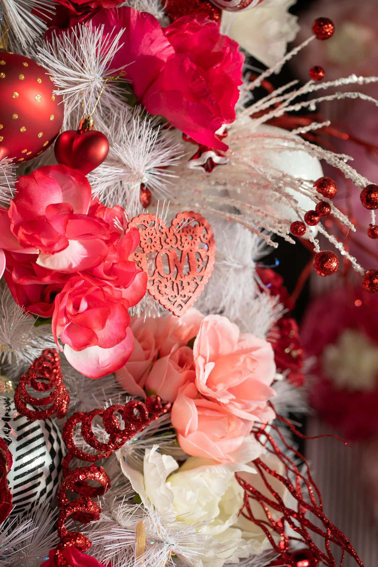 Close up of red heart ornament that says "LOVE"  surrounded by faux roses on a Valentine tree