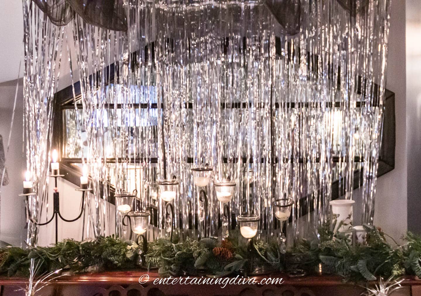 Candles in an evergreen garland with a silver foil curtain behind