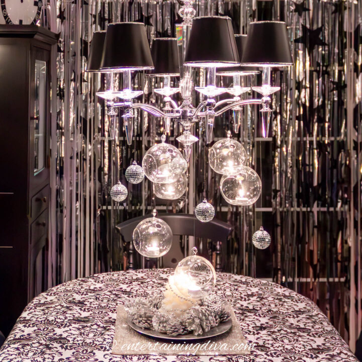 Mini mirror balls and terrariums with white candles hanging from a chandelier with black shades over a black and white table