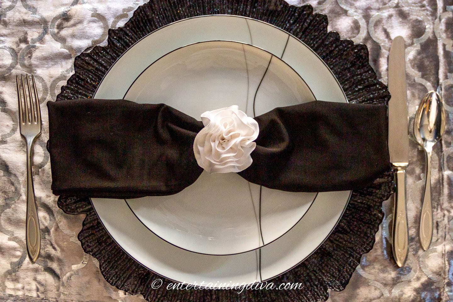Black and white plates and a black napkin with a white napkin ring on a black charger and silver placemat