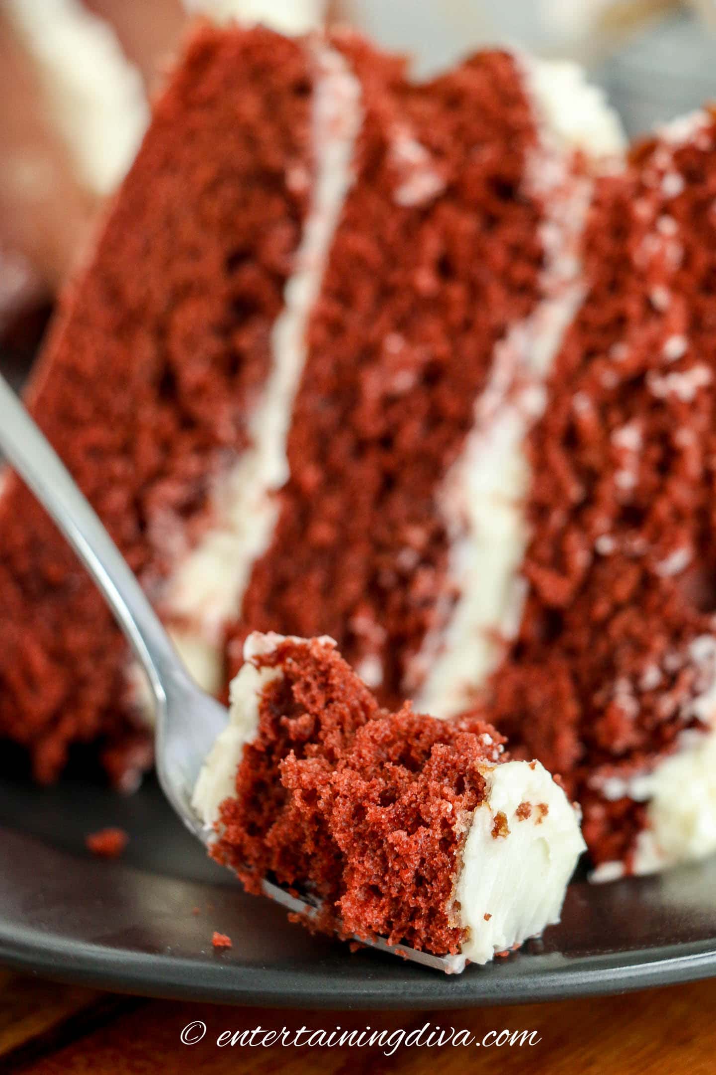 A forkful of Waldorf Astoria red velvet cake in front of a piece of cake