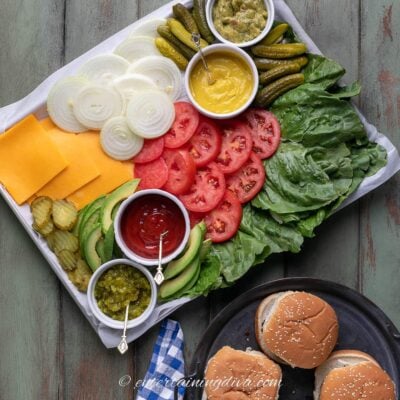 burger toppings charcuterie board beside a plate of hamburgers