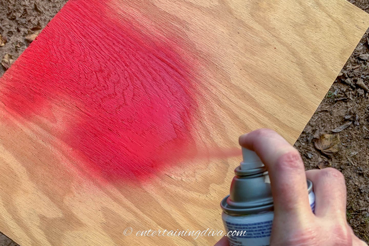 Red spray paint being sprayed on a piece of plywood